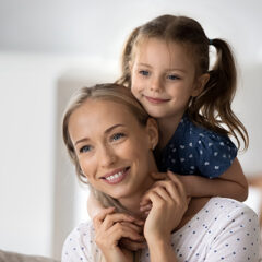 Close up of smiling young Caucasian mother and little daughter hugging cuddling at home. Happy cute small 7s girl child embrace mom show love and care feel grateful thankful. Family concept.